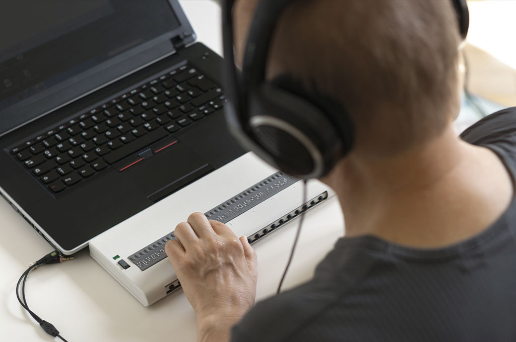 Person an einem Computer mit Screenreader und Braillezeile